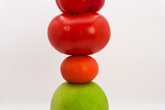Mandarin, apple, tomato and sweet pepper in the form of a tower on a white background, the concept of healthy eating from fruits and vegetables, health care, fruit diet, vegans and vegetables. High qu