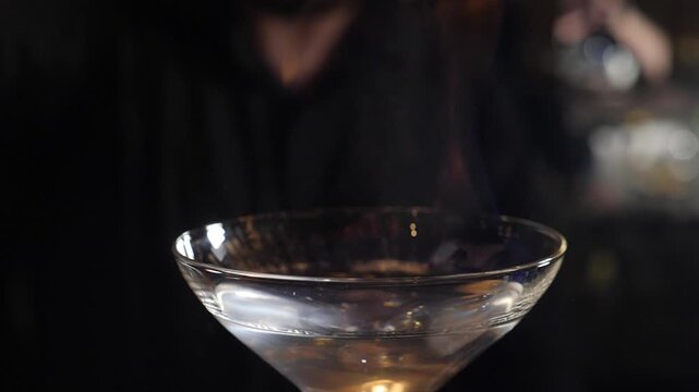 Craft cocktails on bar counter. Bartender sets fire to cocktail, burning cinnamon in alcohol drink on black background. Flames in cocktail glass in slow motion, burning cinnamon in alcohol drink