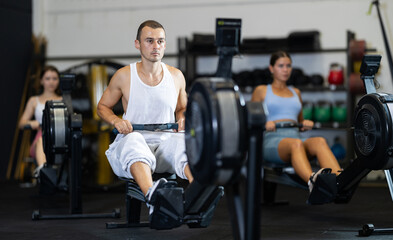 Young athletic man in sportswear training on rowing machine in gym..