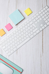 Vertical top view of a modern workspace with white keyboard, colorful sticky notes and green notebook on light wooden desk. Clean minimalist style with copy space. Concept of creative workspace