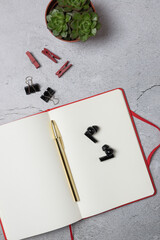 Vertical top view of open notebook with gold pen, wireless earbuds and succulent plant on light gray background. Modern flat lay for creativity, study and work. Concept of creative workspace