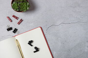 Horizontal top view of open notebook with gold pen, wireless earbuds and succulent plant on light gray background with copy space on the right. Concept of modern workspace