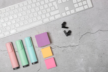 Horizontal flat lay of modern workspace with white keyboard, wireless earbuds, sticky notes and pastel markers on light gray textured background with copy space. Concept of  organization