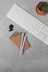 Vertical top view of minimalist desk with keyboard, notebook, pens and cactus on gray stone surface with copy space. Concept of education, social media and professional communication
