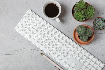 Horizontal top view of modern workspace with white keyboard, coffee cup, succulents and pen on gray stone background. Copy space.  Concept of modern workspace and lifestyle