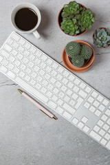 Vertical top view of modern workspace with white keyboard, coffee, succulent plants and pen on gray stone surface. Copy space.  Concept of creative workspace and productivity