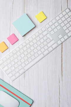 Vertical top view of a modern workspace with white keyboard, colorful sticky notes and green notebook on light wooden desk. Clean minimalist style with copy space. Concept of creative workspace