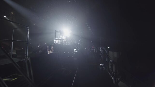 Drummer sits at drums surrounded by strong stage back lights in backstage. Darkness creates contrast during soundcheck in concert hall
