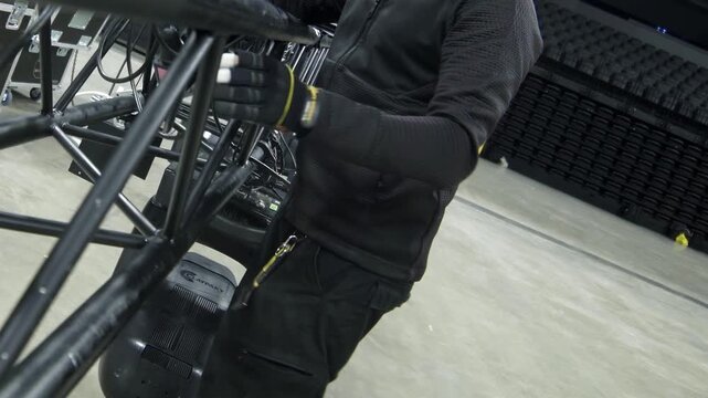 Electrician arranges cables on beam with lamps on stage closeup. Worker connects lighting cords to support equipment in modern concert hall