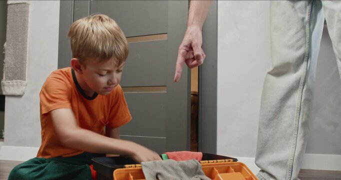 Playful boy opens and closes metal pliers exploring tool mechanics. Father points toward screwdriver inside toolbox guiding child through simple repair interaction