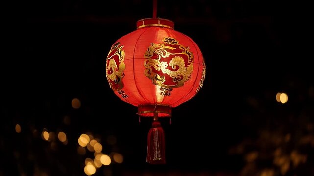 A red lantern with golden designs hangs in a dark area with blurred lights, used for cultural or festive decorations