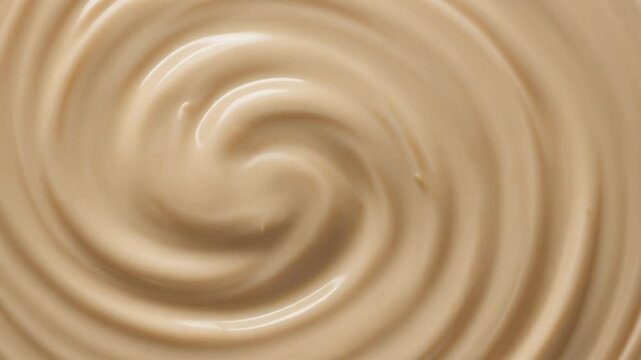 Smooth swirling caramel texture background. close-up of glossy beige cream melted chocolate or coffee latte mix forming an abstract spiral.