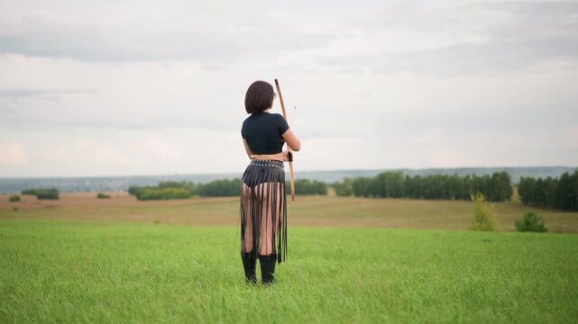 white woman archer draws bow aiming across open green field, leather armguard visible, fringe skirt moving with motion, sequence from draw to release, steady breath and focused posture, training