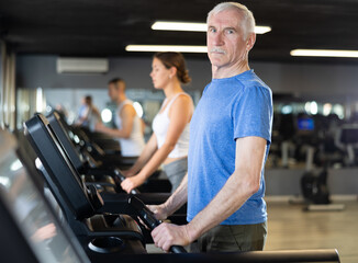 Portrait of elderly man running on treadmill in gym