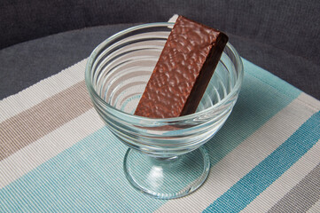 A single chocolate wafer bar rests in a clear glass dessert bowl on a striped placemat