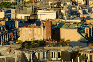Clustered Parisian rooftops featuring classic zinc and slate surfaces, abundant brick chimneys, and rooftop greenery illuminated by golden sunset light.