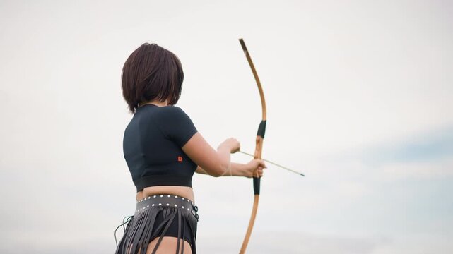 Female archer refining shooting techniques, Woman with bow improving her archery skills diligently, Woman dedicatedly practicing with her bow during cloudy and overcast outdoor environment