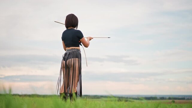 archer woman back view on hill, holding bow and spare arrows with leather quiver, panoramic sky and distant horizon, pensive stance and watchful pose as dusk settles, calm expansive countryside