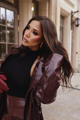 Fototapeta premium beautiful woman with dark hair in elegant leather coat with accessories posing in the street