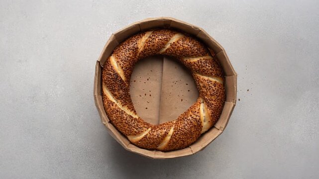 Top view of a traditional Turkish Simit bread with sesame seeds in a brown paper box, slow 360-degree orbit shot, authentic Mediterranean street food 4k video.