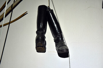 Vintage black leather boots hanging against whitewashed wall