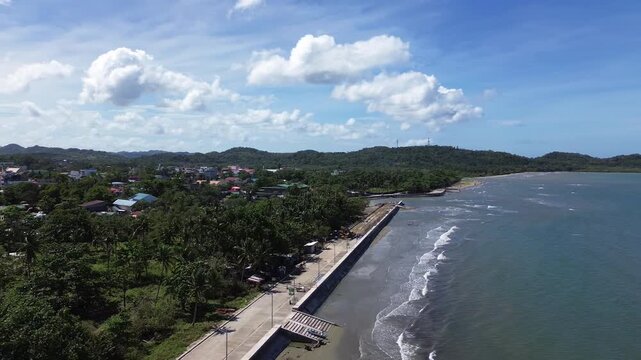 Aerial drone footage of the coastal seawall in Odiongan City on Tablas Island, Philippines, showing a concrete beachfront promenade with palm-lined shoreline, blue sea, and hills in the background.