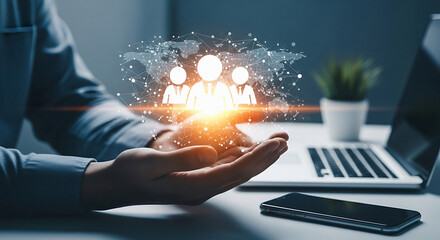 Person holding glowing digital of people in their hand with laptop and smartphone on a desk