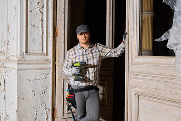 Naklejka premium Worker holds drill while standing by open door in old building