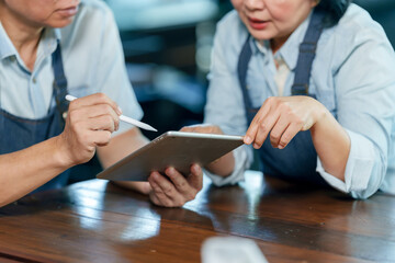 Close up asian senior couple restaurant owners analyzing financial data using tablet teamwork collaboration management communication cooperation cafe small business planning lifestyle concept