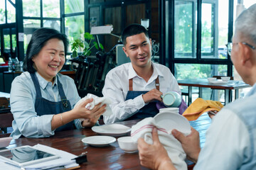 Asian senior female owner laughing with young barista while cleaning dishes teamwork concept cafe restaurant small business cooperation communication family hospitality management friendly working