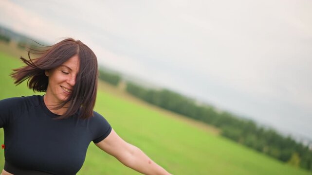 Woman dancing in green field, spinning arms raised wearing black crop top and fringe skirt with combat boots carefree motion, braided hair whipping, closeups of boots and grass, overcast sky,