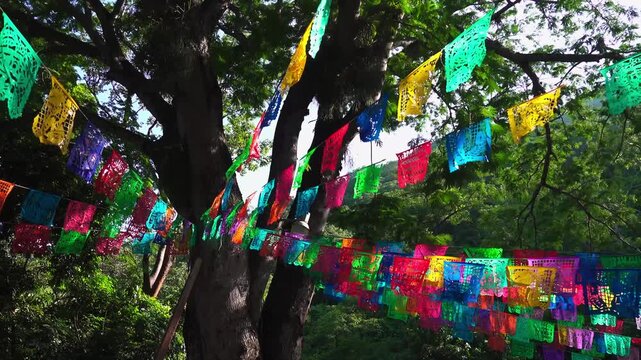 Colorful paper decorations hang from trees in a festive outdoor setting during a celebration in the park