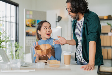 Obraz premium Asian female entrepreneur in blue apron excitedly discussing eco-friendly biodegradable packaging with bearded male partner in sustainable workshop, holding molded pulp tray, creative green business 