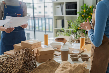Asian entrepreneurs team in sustainable workshop discussing eco-friendly biodegradable packaging, holding molded pulp trays and kraft boxes,creative green business startup collaboration bright room
