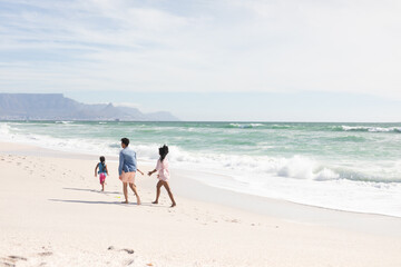 Full length of multiracial parents walking behind son on shore at beach during sunny day
