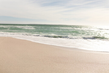 Waves in sea crashing on shore at beach against sky during sunny day
