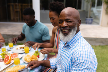 Portrait of smiling bearded bald african american senior man eating brunch with family at backyard © wavebreak3