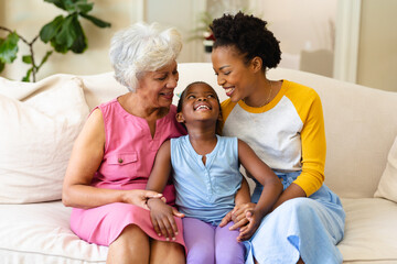 African american grandmother, mother and granddaughter smiling looking at each other at home