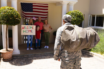 Caucasian military soldier with bag returning home walking towards family with welcome placard