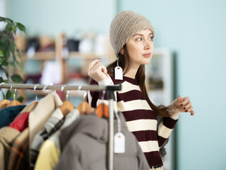 Undecided young woman looking for warm hat in retail outlet with new winter collection