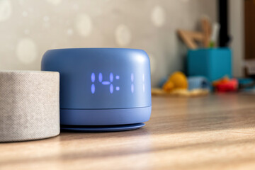 Modern blue digital clock and smart speaker on a wooden table in a contemporary home setting. Essential smart home technology and convenience