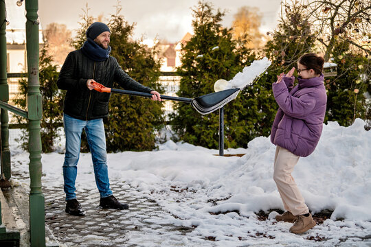 man, shoveling snow, playfully throws snow at teenage daughter,