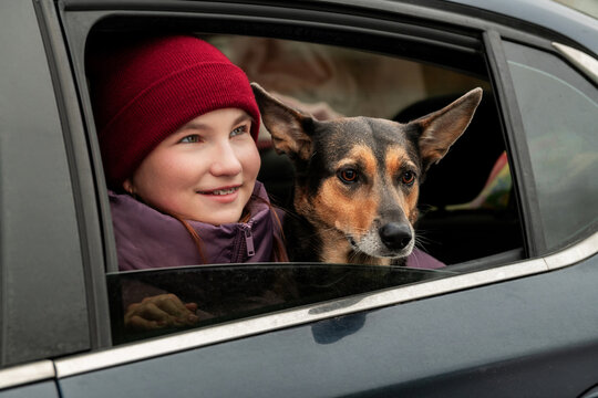teenage girl and dog peeking out of car window during winter trip.