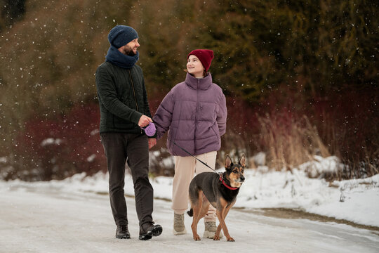 Teenage girl and man walking dog on a snowy path in winter park.