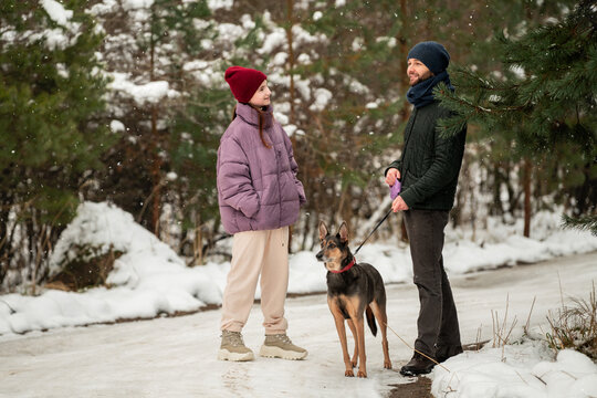 Teenage girl and man walking dog on a snowy path in winter park.