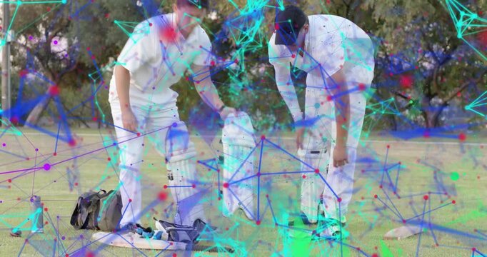 Two male cricket players sorting kit and strapping pads, network overlay passing, preparing to bat