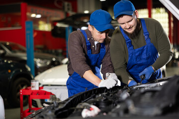 Two skilled male auto mechanics in blue overalls repairing automobile in car workshop