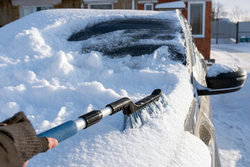 snow removal of the car. A man is holding a snow cleaning brush.