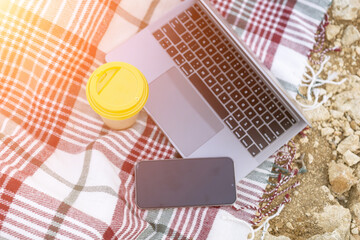 Laptop on blanket with ocean view. Illustrating serene outdoor laptop use. Freelancer enjoying their time outdoors while working or browsing the internet.