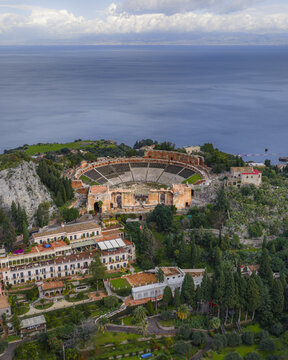 Aerial view of the ancient Teatro Antico stands in stark contrast against the azure sea, a symphony of stone and sky, Taormina, Sicily, Italy.